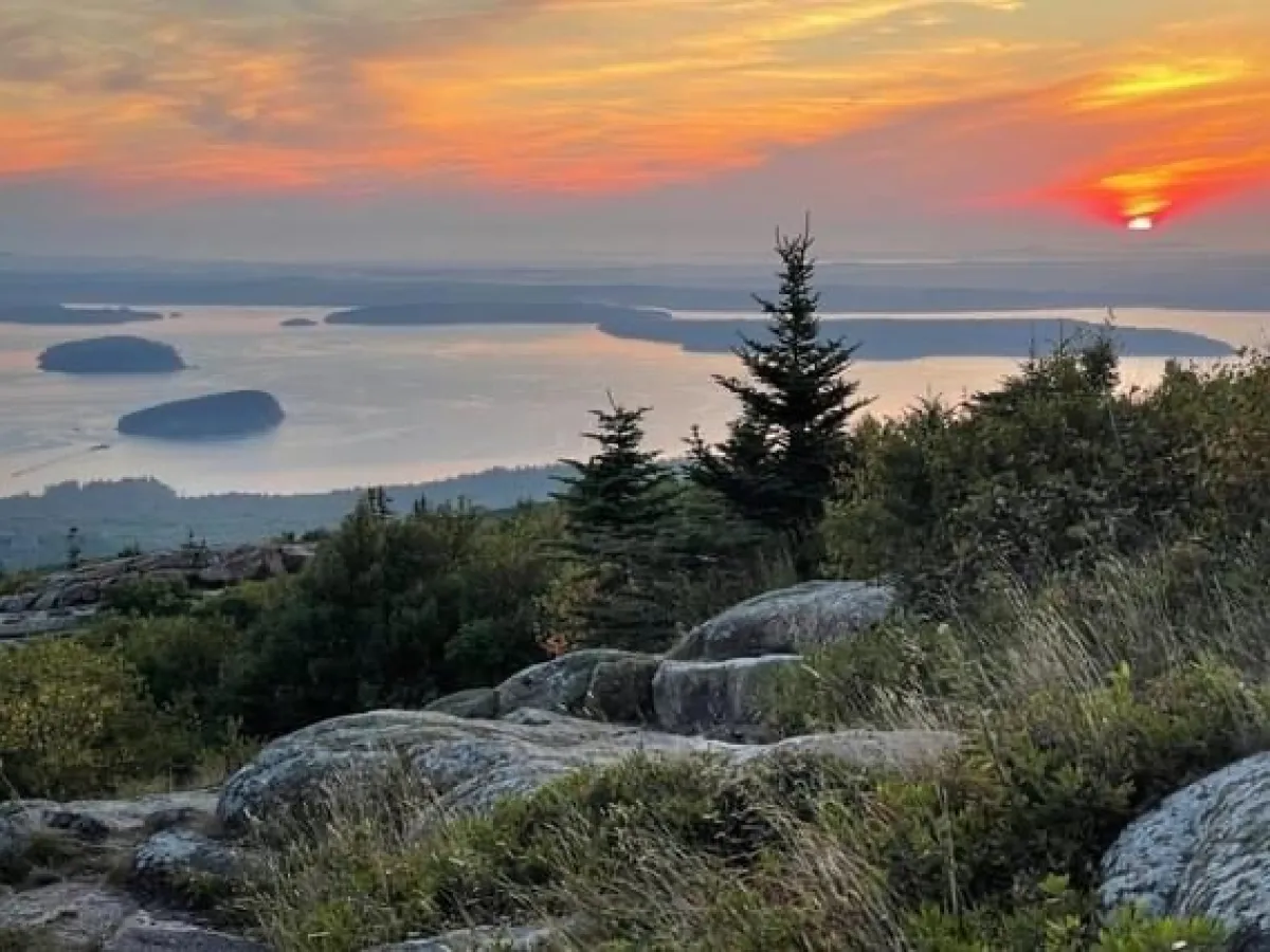 Sunrise over a rocky landscape and distant islands in a calm sea.