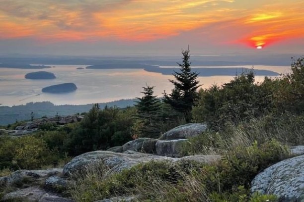 Sunrise over a rocky landscape and distant islands in a calm sea.