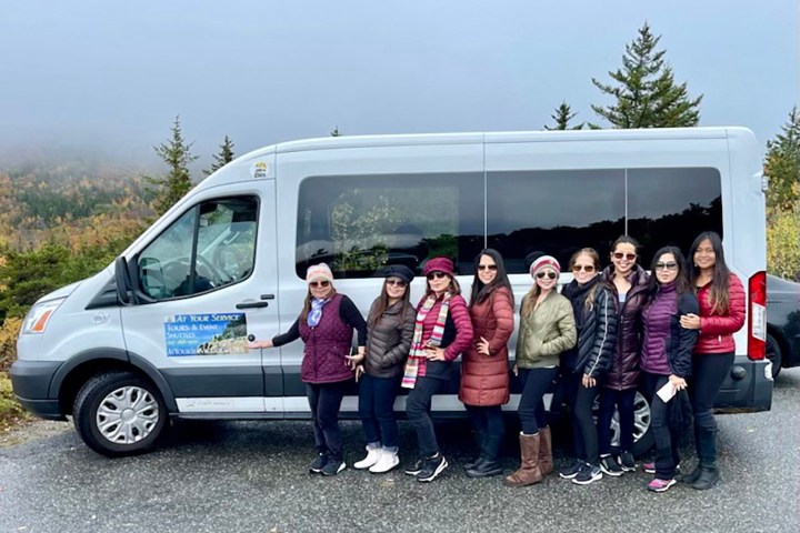 Group of people posing beside a gray van with trees and foggy background.