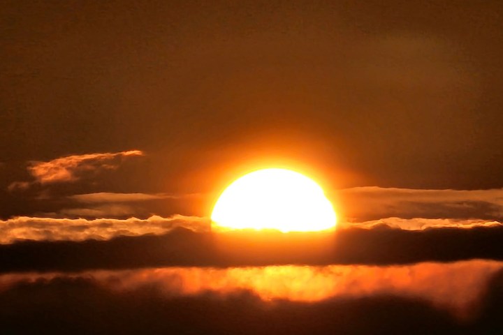 Sun setting behind dark clouds with orange glow.